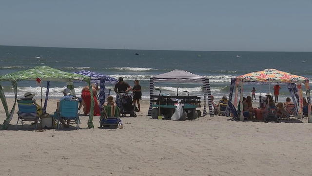 People site under tents on the beach in Margate, New Jersey, on a sunny day. The ocean stretches out in the background 